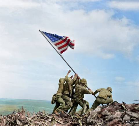 Un grupo de soldados levanta la bandera de Estados Unidos en un campo de batalla.