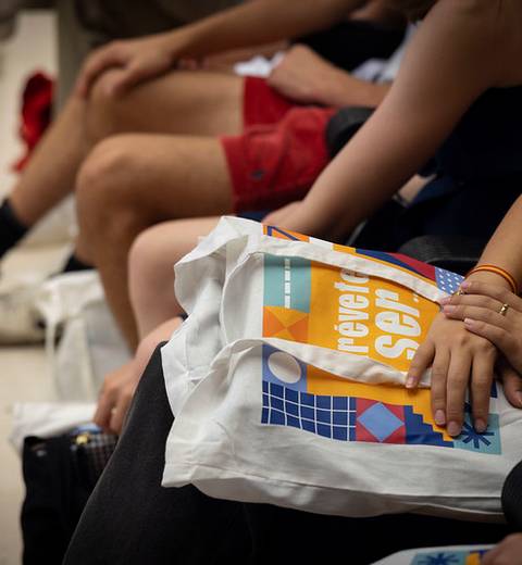 Un grupo de personas sentadas en una fila sosteniendo bolsas de tela con un diseño colorido.