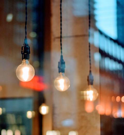 La imagen muestra bombillas colgantes iluminando un ambiente urbano reflejado en una ventana.