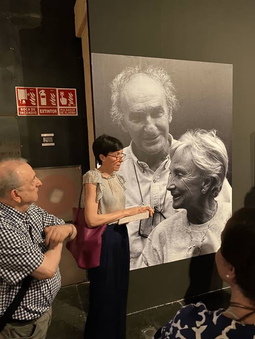 En la imagen, un grupo de personas observa una fotografía en blanco y negro de dos ancianos sonriendo juntos.