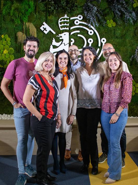 A group of six people smiling and posing in front of a decorative wall with graphic designs.