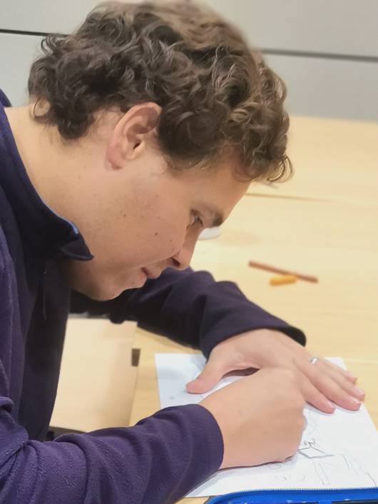 A young man is focused on writing or drawing on a sheet of paper at a table.