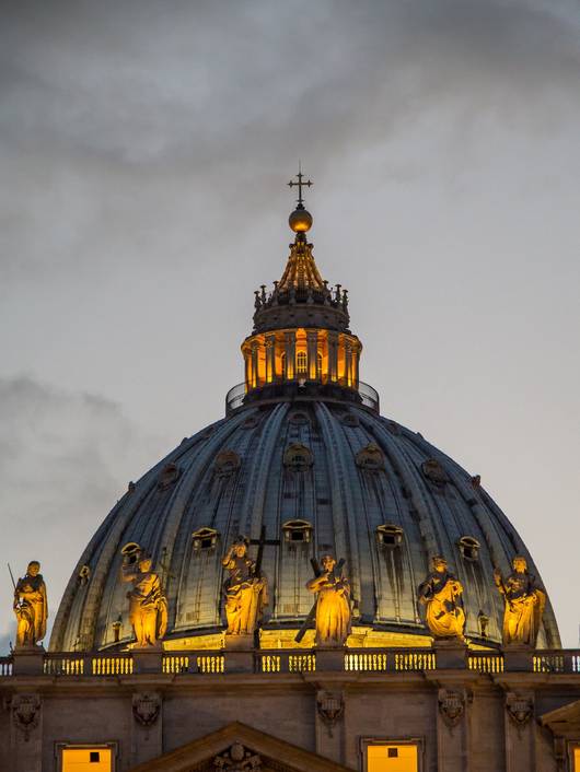 La imagen muestra la cúpula de la Basílica de San Pedro iluminada al atardecer.