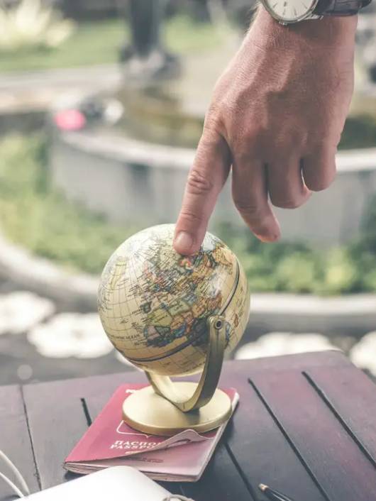 Una mano señala un globo terráqueo sobre una mesa en un entorno natural.