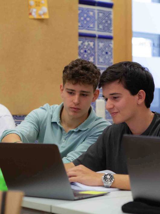 Tres jóvenes estudiantes trabajan en sus computadoras portátiles en un aula.