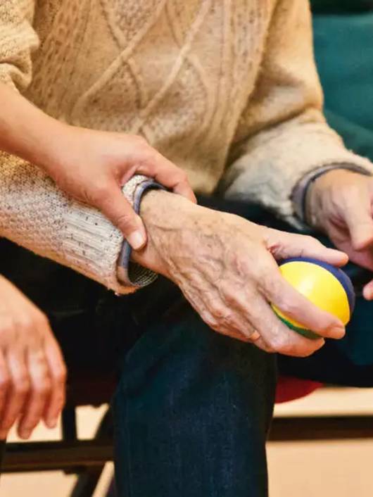 Una persona mayor sostiene una pelota mientras recibe apoyo de otra persona.