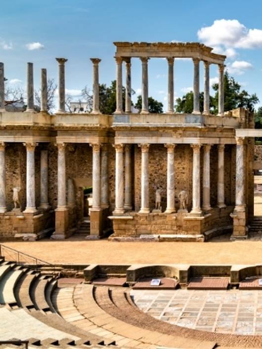Ruinas de un antiguo teatro romano con columnas y un escenario visible.