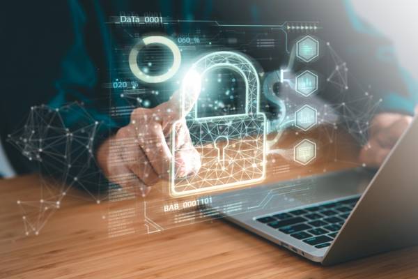 A person interacts with a futuristic cybersecurity interface on a laptop, showing graphs and security symbols.