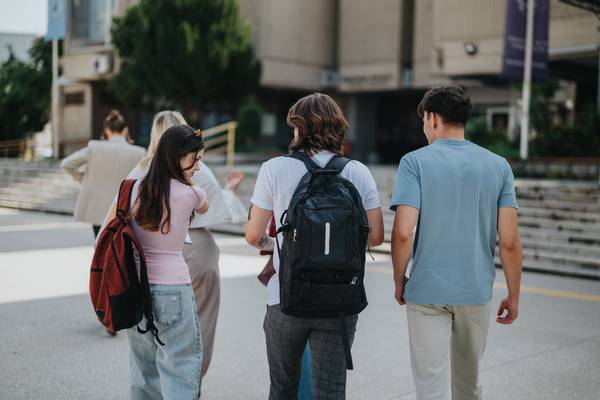 Un grupo de jóvenes camina juntos hacia un edificio con mochilas en la espalda.