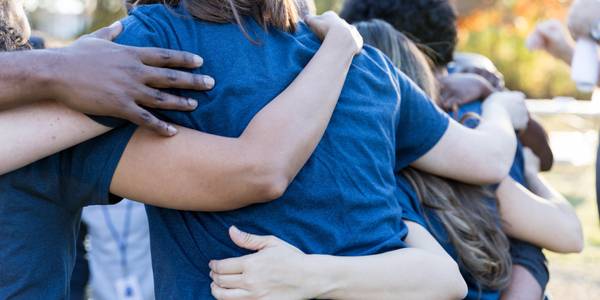 A group of people in blue shirts embracing in a group hug outdoors.