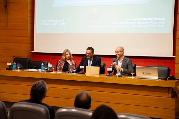 Una conferencia con tres ponentes sentados en una mesa compartiendo información.