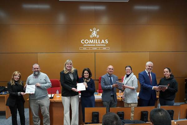 Fotografía de un evento en la Universidad Pontificia Comillas donde varias personas posan sosteniendo documentos.