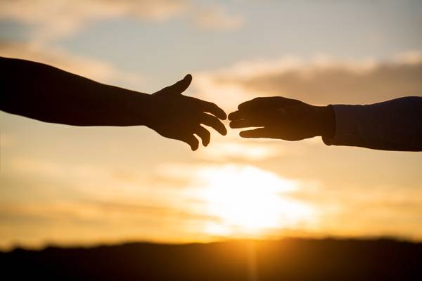 Silhouettes of two hands reaching towards each other against a sunset background.