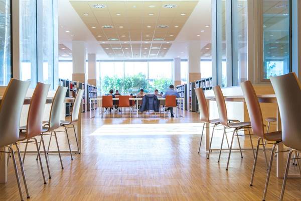 Una vista interior de una sala de estudio con mesas y sillas, donde varias personas están concentradas en su trabajo.