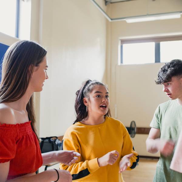 Tres jóvenes conversan animadamente en un entorno interior.