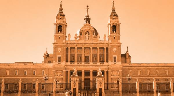 La imagen muestra una gran edificación de estilo arquitectónico majestuoso, iluminada por un tono naranja.