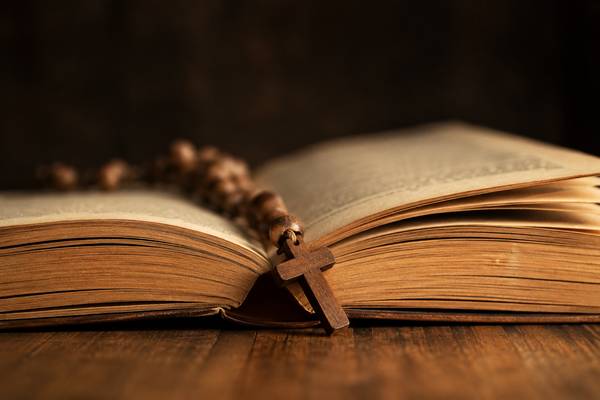 Un libro abierto con un rosario y una cruz en la parte superior.