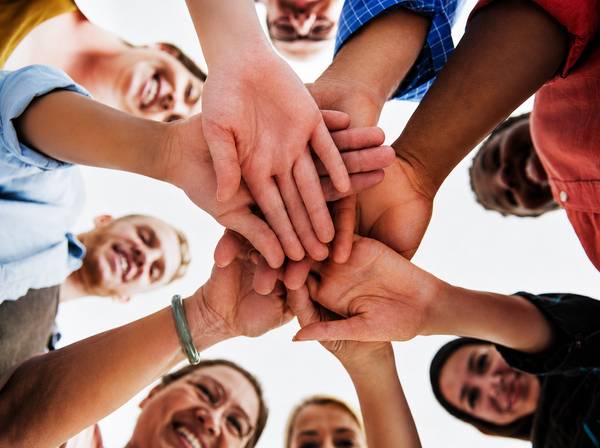 Un grupo de personas está uniendo sus manos en el centro de la imagen, simbolizando unidad y colaboración.