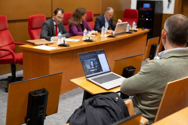 Un grupo de personas se reúne en una sala con mesas y sillas, mientras un asistente usa una computadora portátil.