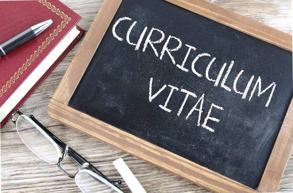 A chalkboard with the words 'curriculum vitae' written on it, placed on a wooden surface next to glasses and a red notebook.