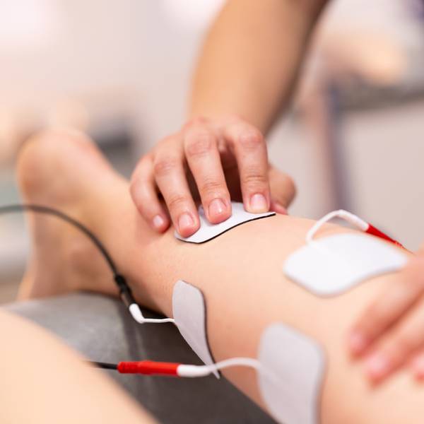 A person receiving electrical stimulation therapy on their knee with electrode pads attached.