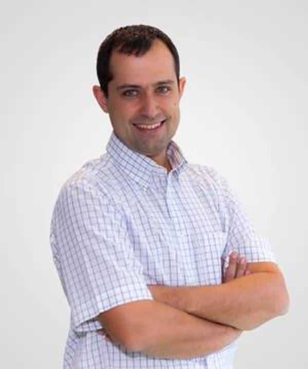 A man in a checkered shirt smiling at the camera with his arms crossed.