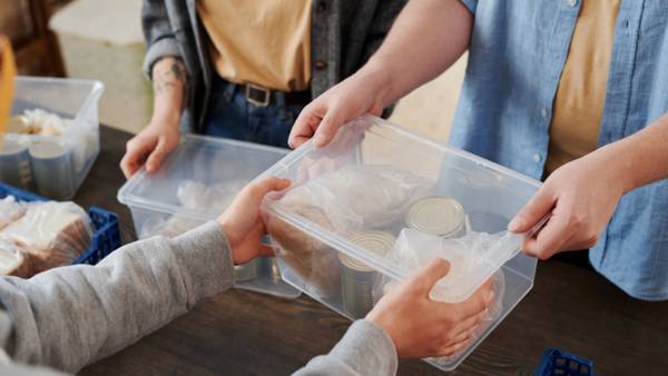 Un grupo de personas está intercambiando cajas transparentes con alimentos en un entorno comunitario.