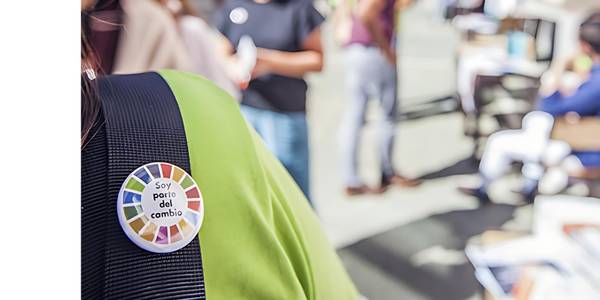 A close-up of a badge reading 'Soy parte del cambio' pinned on a person's shirt in a bustling office environment.