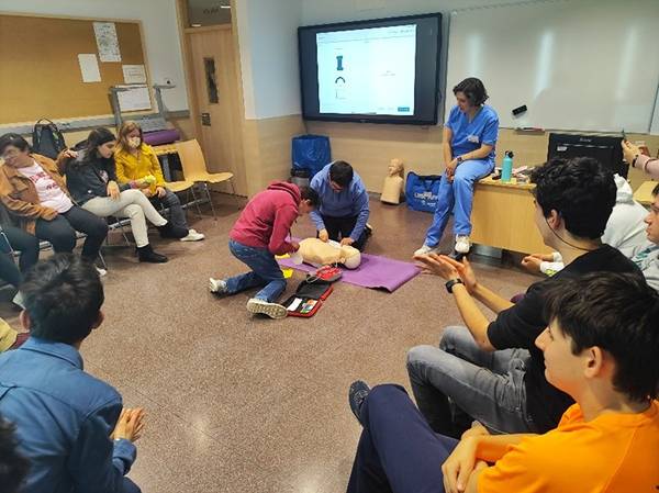 Un grupo de personas observa mientras un muchacho realiza maniobras de reanimación cardiopulmonar en un muñeco de prácticas.