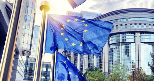 Una imagen de varias banderas de la Unión Europea frente a un moderno edificio.