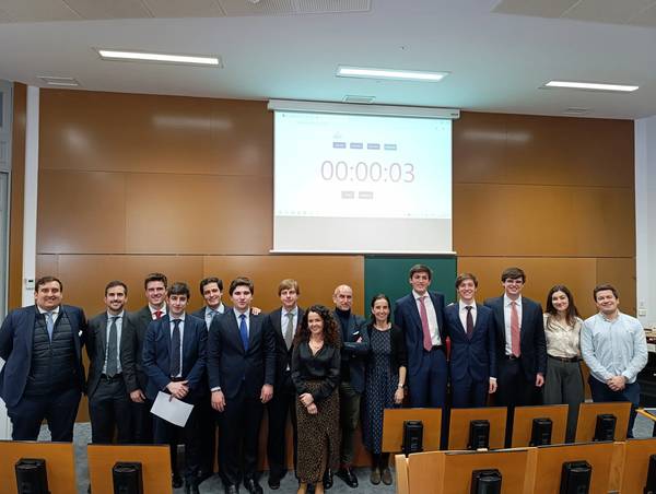 Grupo de personas vestidas formalmente posando en un aula con un temporizador en el fondo.