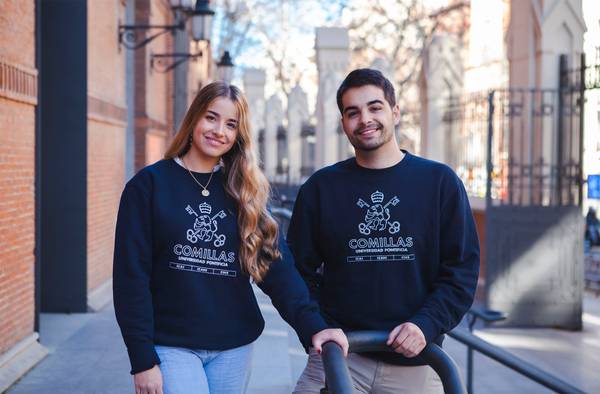 Dos jóvenes posan en un entorno urbano vistiendo sudaderas, sonriendo y mostrando un ambiente amigable.
