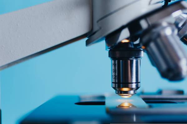 La imagen muestra un microscopio con un fondo azul claro.