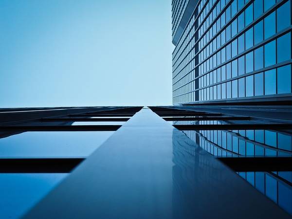 Vista desde abajo de un edificio moderno con ventanas reflejantes bajo un cielo azul.