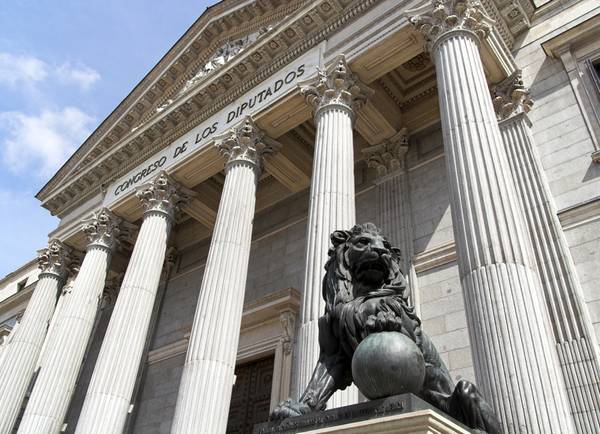 La imagen muestra la fachada del Congreso de los Diputados en Madrid, destacando una escultura de un león en primer plano.
