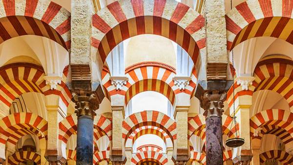 La imagen muestra un interior arquitectónico con arcos de colores rojo y blanco, típicos de la tradición islámica en España.