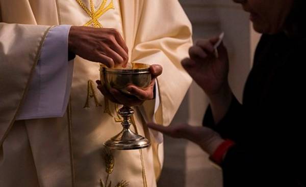 Un sacerdote con vestiduras litúrgicas sostiene un cáliz mientras una persona extiende la mano.