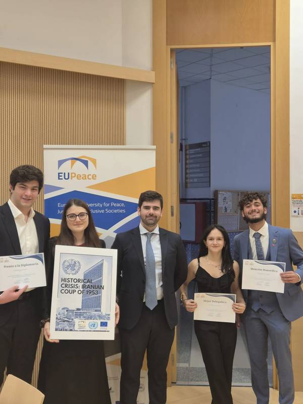Un grupo de cinco personas posan con certificados y una presentación en un evento relacionado con la paz en Europa.