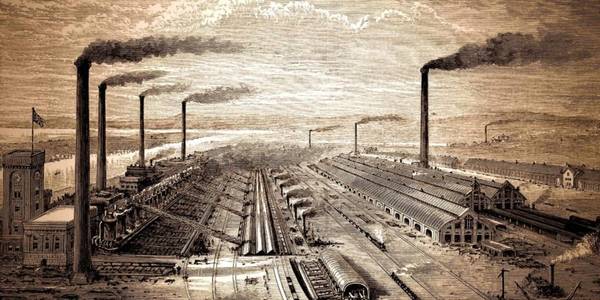 Una vista panorámica de una zona industrial con chimeneas humeantes y vías de tren.