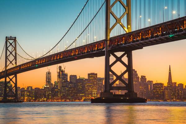La imagen muestra el atardecer sobre la ciudad de San Francisco con el puente de la Bahía en primer plano.