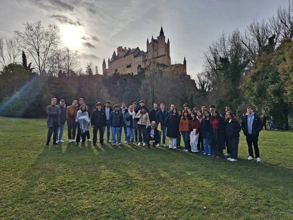 Un grupo de personas posando en un campo con un castillo al fondo y un cielo nublado.