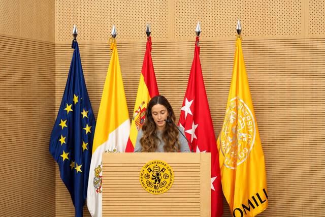 Una mujer habla en un podio ante varias banderas en un evento oficial.