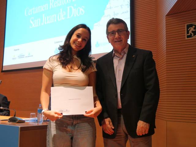 Una mujer sonriente sostiene un certificado junto a un hombre en un evento.