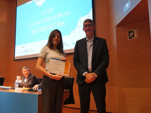 La imagen muestra a una mujer recibiendo un premio durante un evento relacionado con relatos breves, mientras un hombre la acompaña en el escenario.