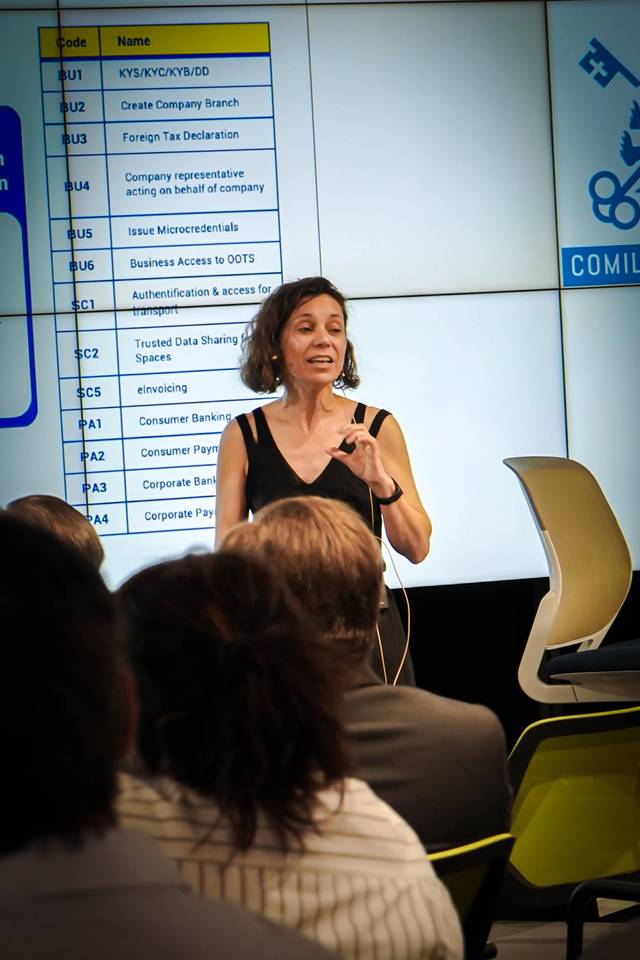 Una mujer está presentando información en una pantalla mientras un público la observa.