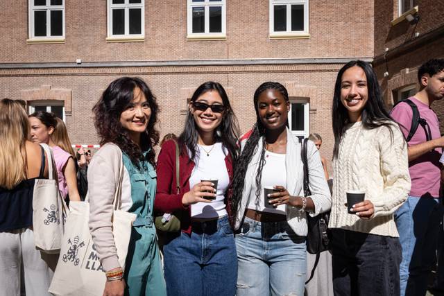 Un grupo de cuatro mujeres sonrientes sostiene vasos en un evento al aire libre.