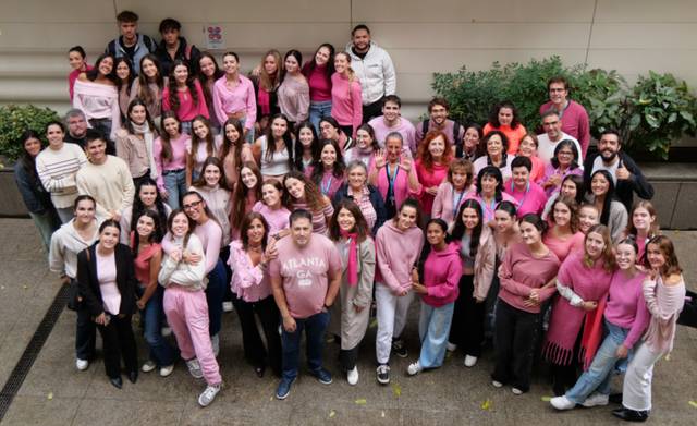 Un grupo grande de personas posando juntas, la mayoría vestidas de rosa, en un ambiente al aire libre.