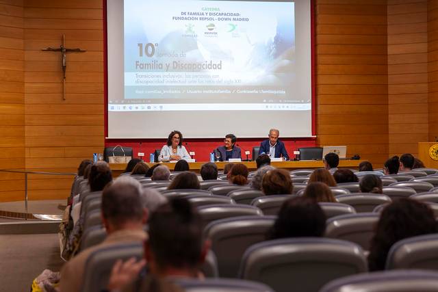 People attending a conference with speakers presenting on stage in a lecture hall.