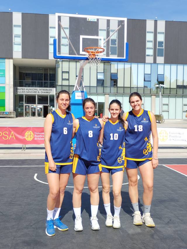 Four female basketball players posing on an outdoor court in front of a basketball hoop, dressed in matching blue and yellow uniforms.