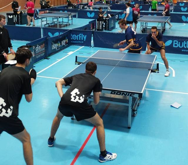 Players engaged in a table tennis doubles match in an indoor sports hall.
